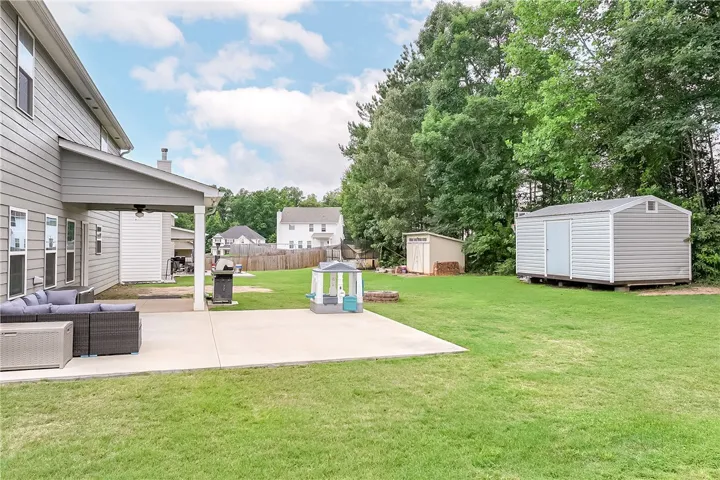 A spacious, green yard offers a covered patio and two versatile storage sheds, ideal for outdoor living.