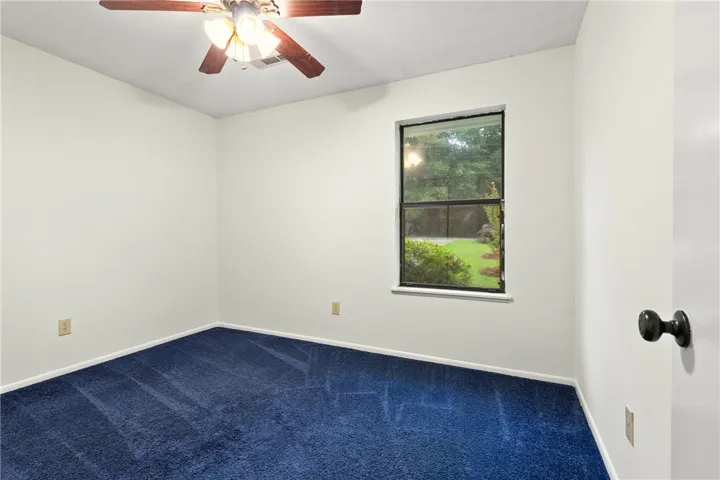 A well-lit bedroom with fan & plush blue carpeting, also double door closet.