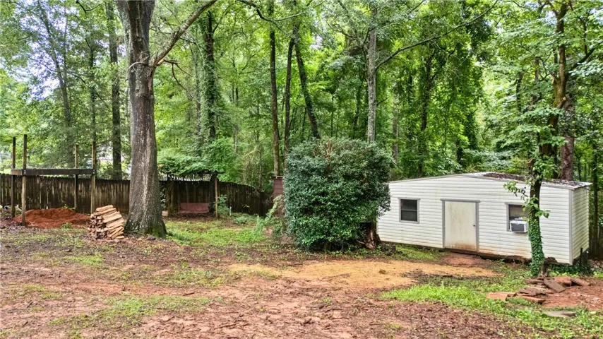 A tranquil wooded backyard features a workshop or additional storage & wood fence.