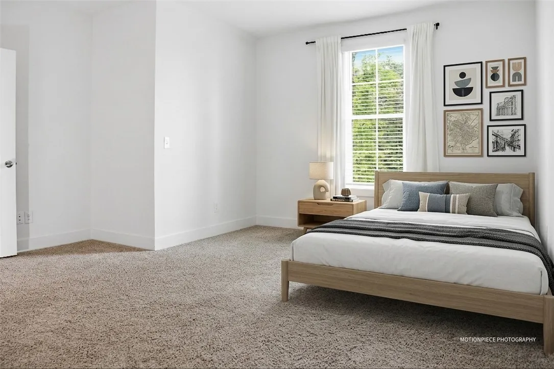 A restful bedroom offers soft carpeting and ample natural light through a large window.