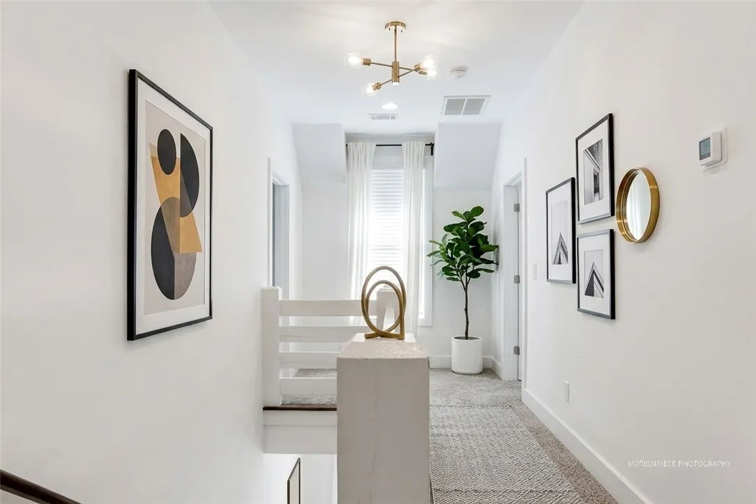 A well-lit landing and hallway features carpeting, a contemporary chandelier, and bright window treatments.