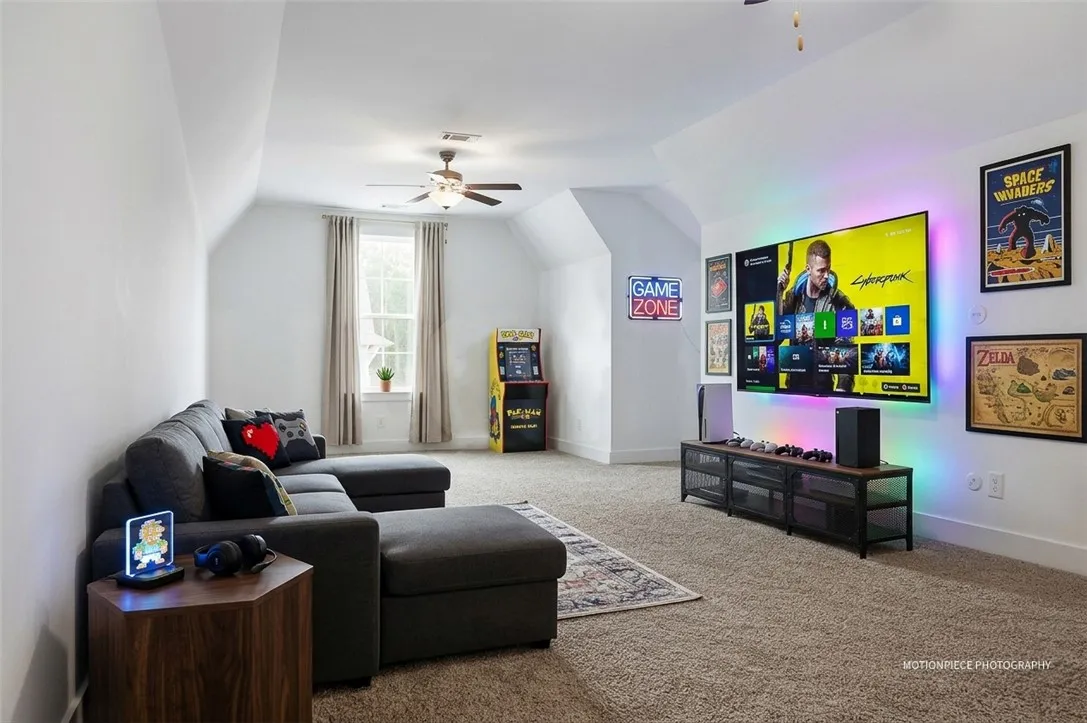 A well-lit game room features soft carpet, a sectional sofa, and a large display.