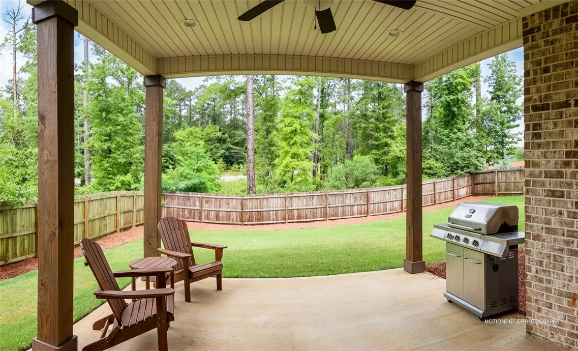 A spacious covered patio invites relaxation with views of a fenced, well-maintained yard bordered by natural woodlands.