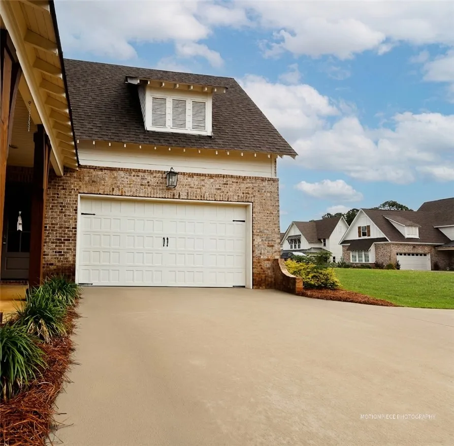 A well-maintained concrete driveway leads to a charming brick-faced garage with a dormer window.