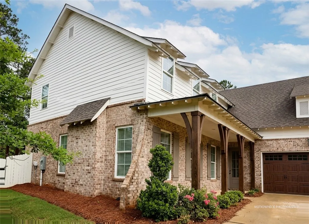 Crafted with classic brick and white siding, this home features an inviting covered porch supported by substantial wooden columns.