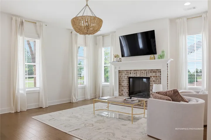 A well-lit living space features rich hardwood flooring and a classic brick fireplace.