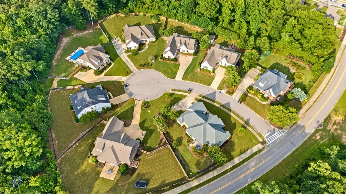 An aerial view captures a quiet cul-de-sac neighborhood surrounded by lush, mature trees.