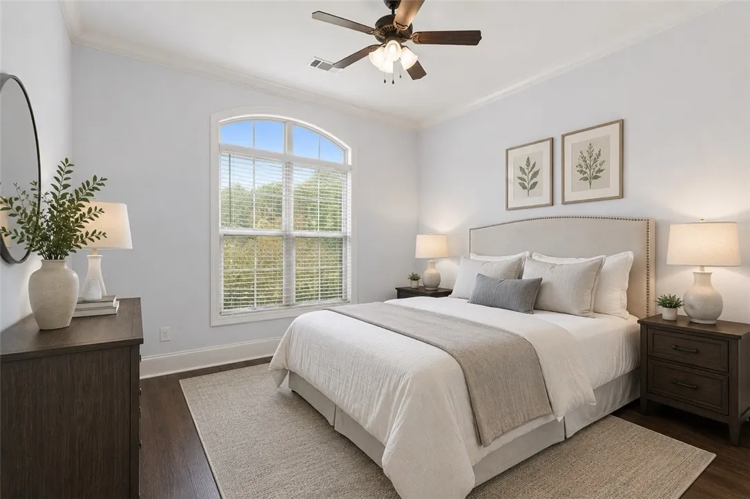A well-lit downstairs bedroom features hardwood floors, a prominent arched window, and an inviting ambiance. Virtually staged