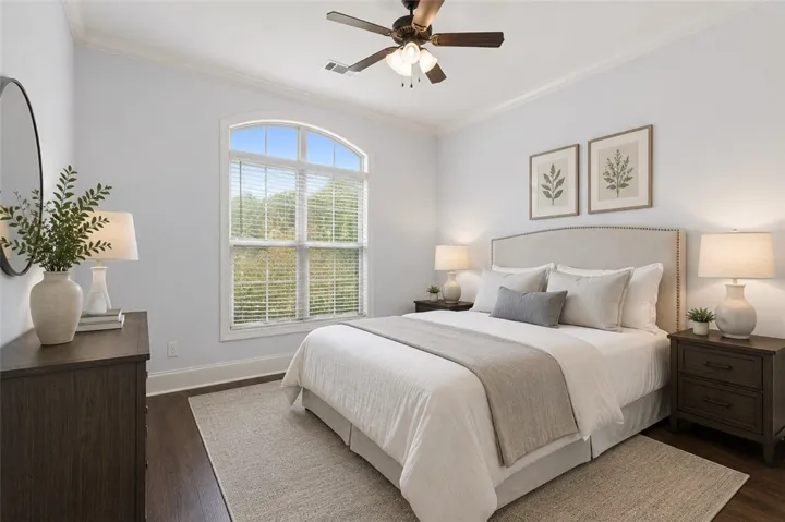 A well-lit downstairs bedroom features hardwood floors, a prominent arched window, and an inviting ambiance. Virtually staged