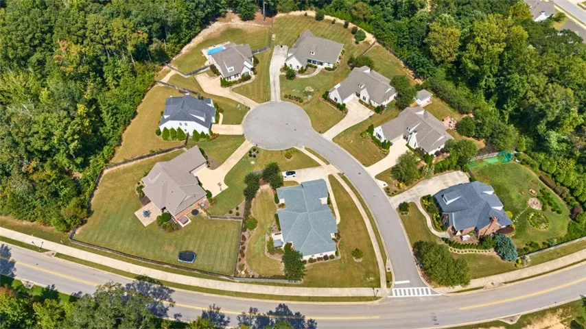 An aerial perspective reveals a serene cul-de-sac neighborhood bordered by mature woodlands and featuring spacious, well-maintained yards.