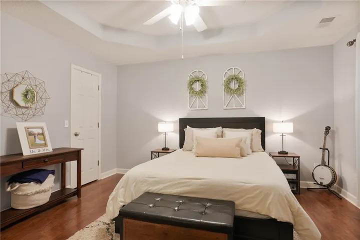 A well-lit primary bedroom features a tray ceiling, hardwood flooring, and a ceiling fan for comfort.