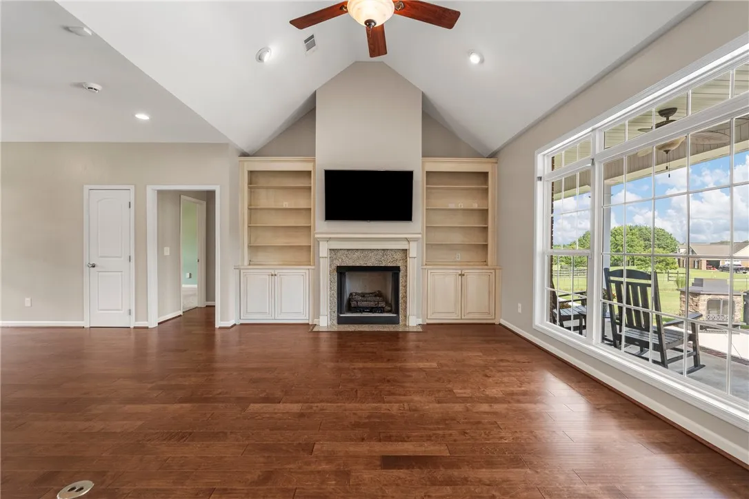 A spacious great room showcases soaring vaulted ceilings and rich wood flooring, featuring a cozy fireplace flanked by built-in shelving.