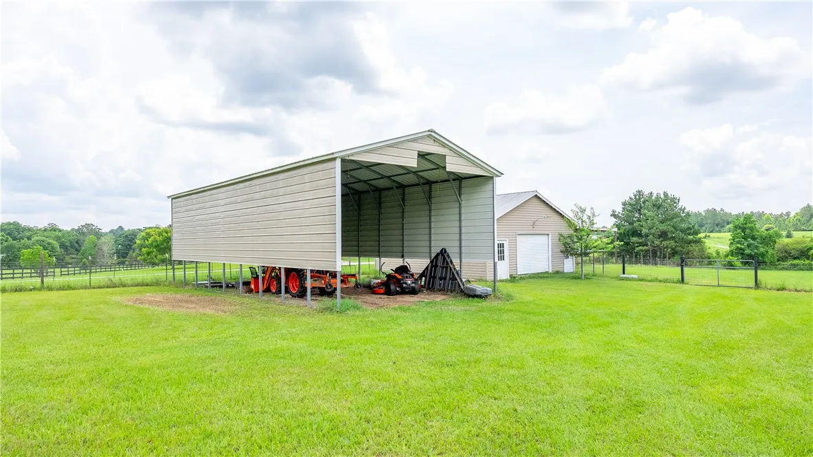 A spacious metal carport and detached garage offer ample storage for outdoor equipment on a sprawling green estate.