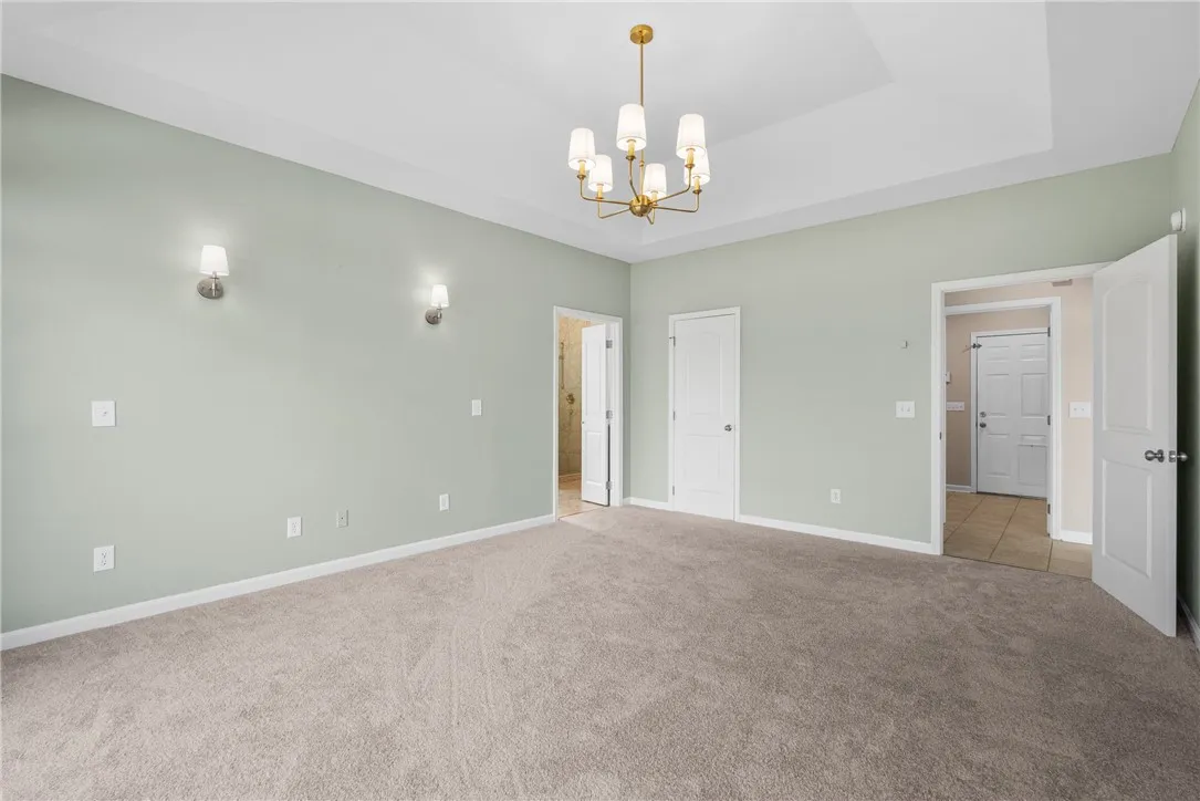 A spacious primary bedroom features soft carpeting, a high tray ceiling, and dual doorways leading to adjoining spaces.