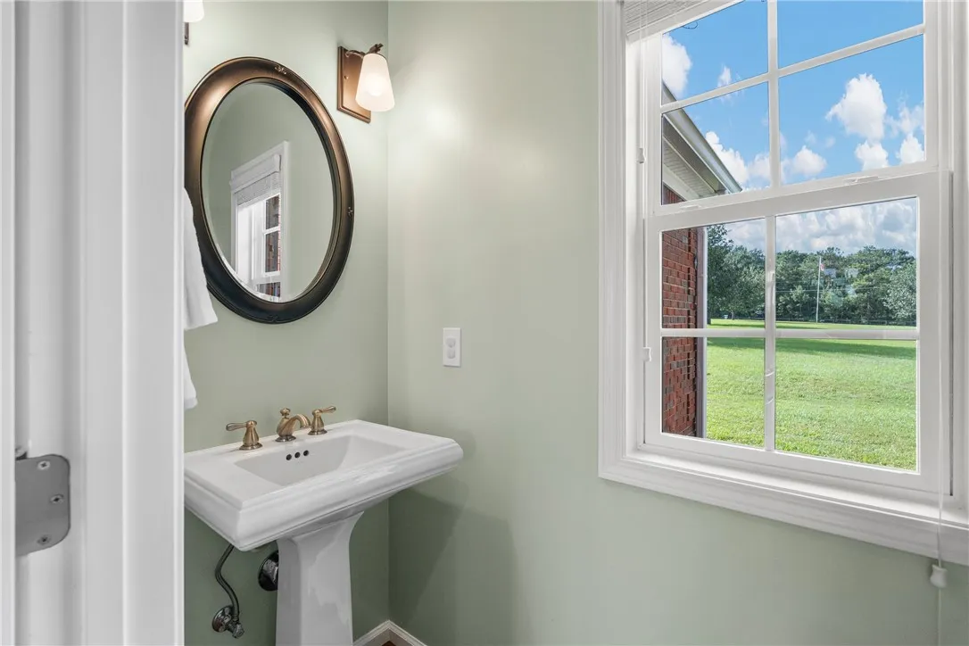 A window-lit bathroom with a classic pedestal sink and an elegant oval mirror.
