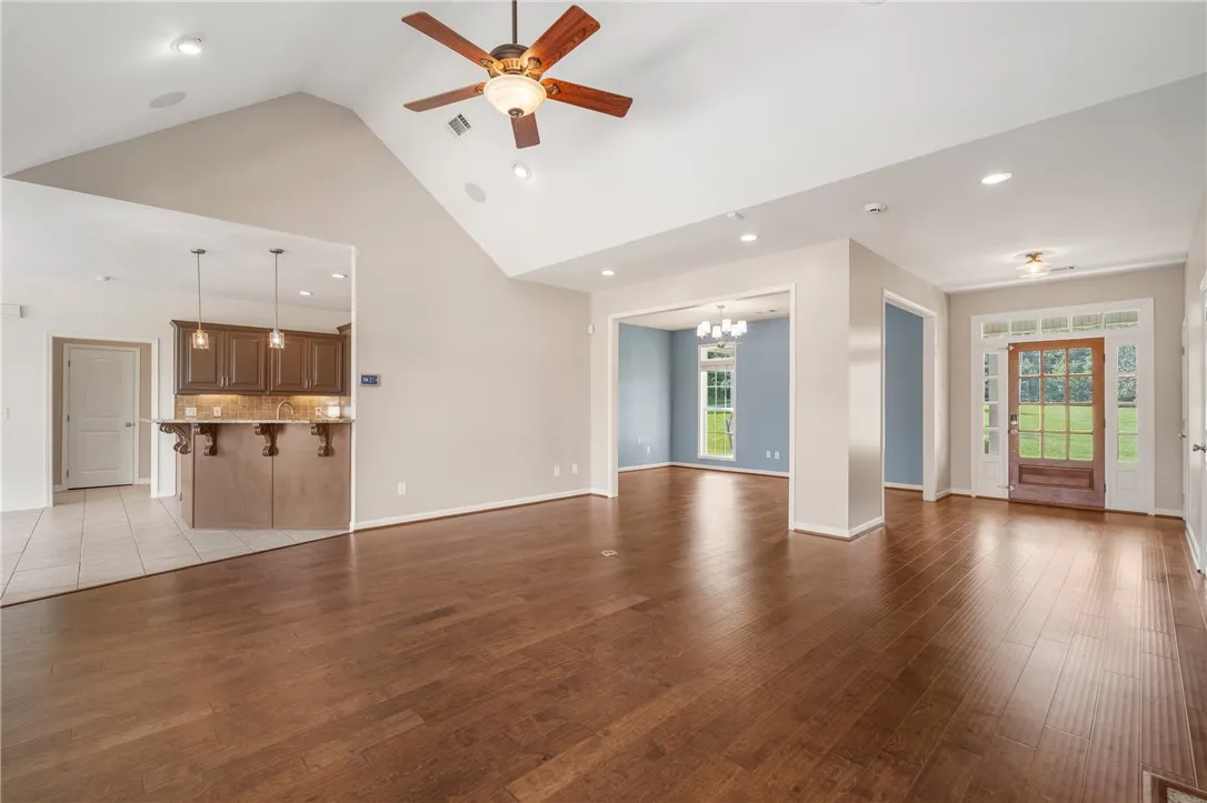 Gleaming hardwood floors flow throughout this inviting open-concept living space, boasting high vaulted ceilings and a clear view to the dining area.