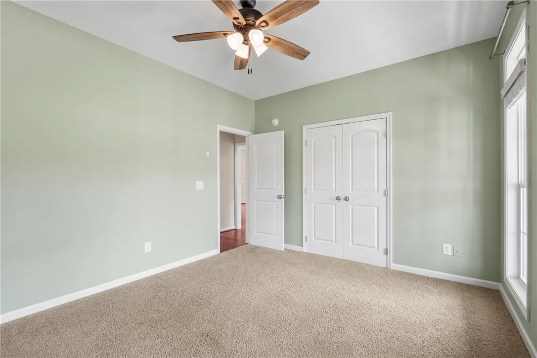 A well-lit bedroom features plush carpeting and a convenient ceiling fan for comfort.