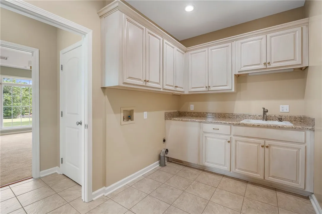 Functional laundry room equipped with ample cabinetry, a utility sink, and granite countertops.