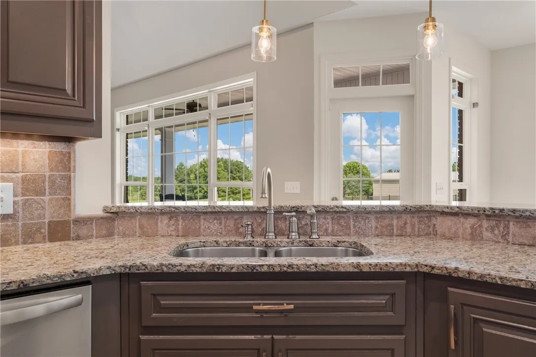 A well-appointed kitchen features rich cabinetry, granite countertops, and a dual basin sink, complemented by clear glass pendant lighting.