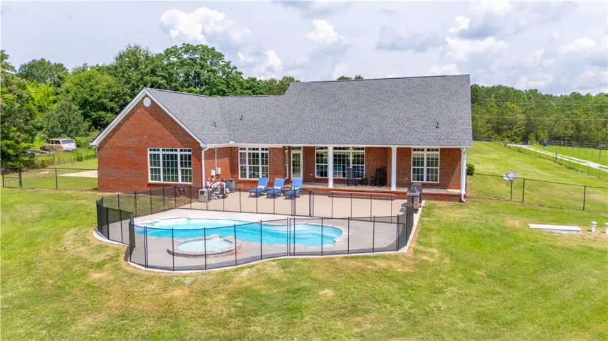 An inviting brick dwelling boasts a covered porch and an in-ground pool with an adjacent spa.