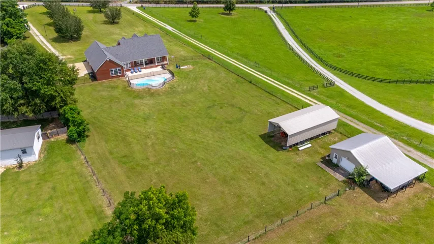 An aerial perspective reveals a private residence with a shimmering pool, accompanied by versatile outbuildings amidst verdant grounds.