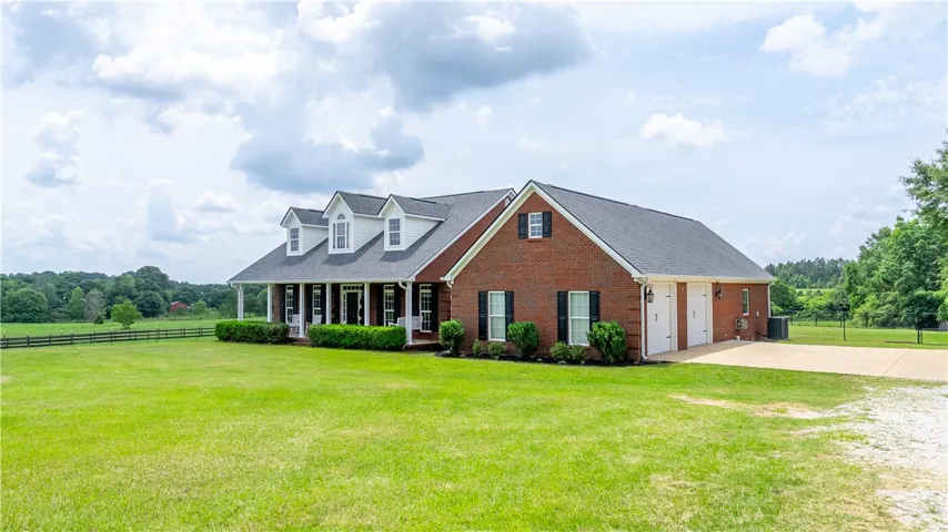 A classic brick exterior with a welcoming porch and abundant green space offers serene country living.