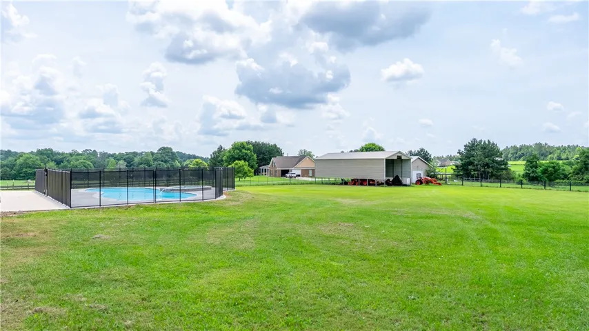 A spacious backyard unfolds with a fenced swimming pool and outbuildings against a backdrop of lush greenery.