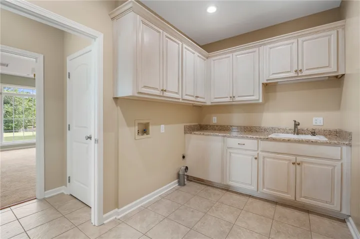Functional laundry room equipped with ample cabinetry, a utility sink, and granite countertops.