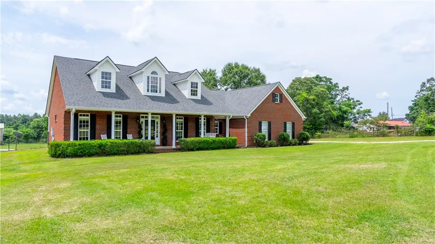 A classic brick-front residence with a deep, welcoming porch overlooks a vast green lawn.
