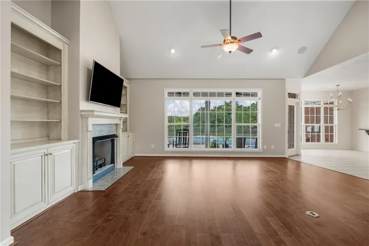 A spacious living area with rich wood flooring opens to a scenic outdoor pool vista.