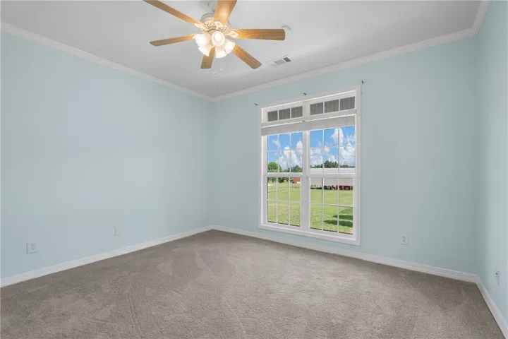 A spacious room offers comfortable carpeted flooring, a practical ceiling fan, and ample natural light from a large window.