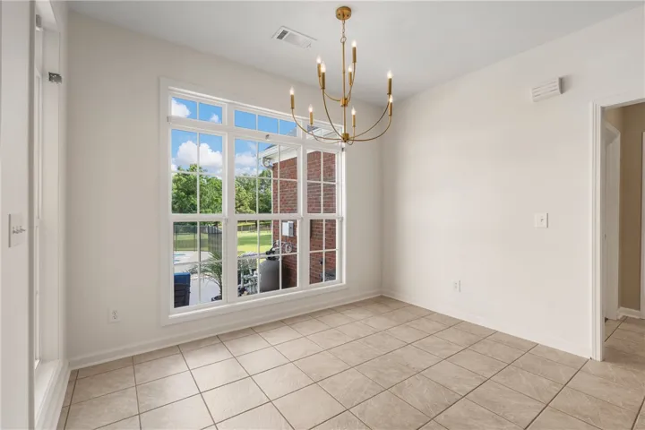 A refined dining space with ample natural light, tile flooring, and a contemporary brass chandelier.