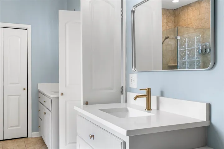 A well-appointed bathroom features a single vanity with a sleek white countertop, complemented by a stylish bronze faucet and a modern mirror.