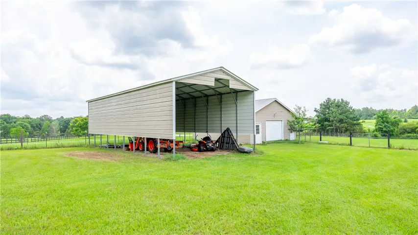 A spacious metal carport and detached garage offer ample storage for outdoor equipment on a sprawling green estate.