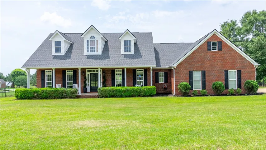 Timeless brick residence featuring a broad front porch and classic dormer windows, framed by lush greenery.