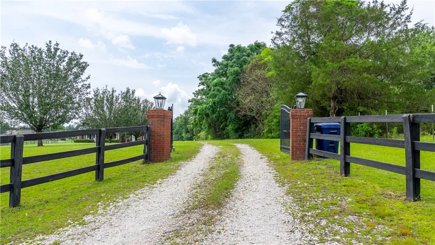 A long gravel driveway guides visitors to a secluded estate, framed by a handsome fence and mature trees.