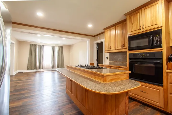 A galley style kitchen with rich wooden cabinetry, built-in range, functional island and stainless appliances.