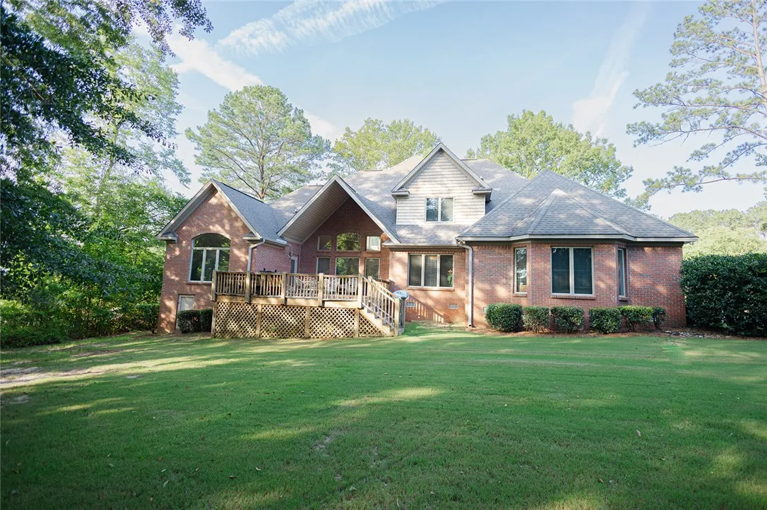 A spacious backyard with mature trees surrounds this inviting brick home, featuring a large deck perfect for outdoor gatherings.