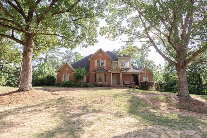 Mature trees shade a welcoming brick residence, showcasing a classic front porch with ample space.