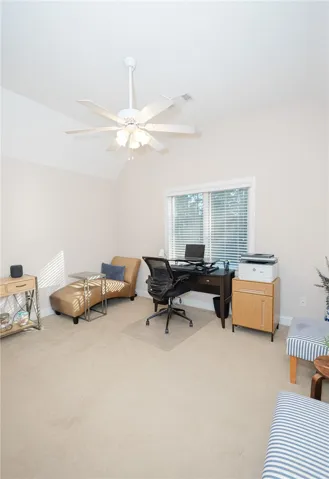 A well-lit study with a vaulted ceiling and soft carpeting creates an ideal home office environment.