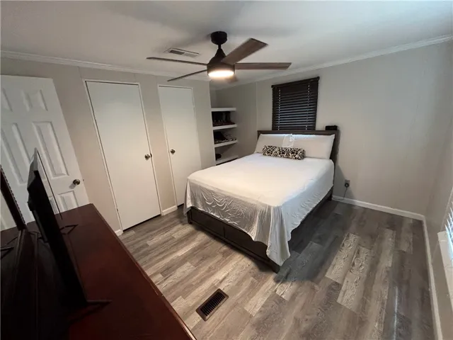 Relax in this tranquil bedroom, featuring a warm wooden-toned floor and a modern ceiling fan.