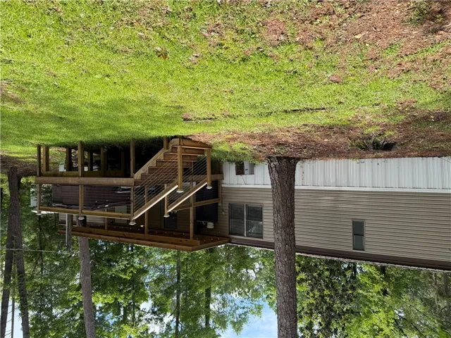 A spacious elevated deck with cable railings extends from this inviting siding home, surrounded by verdant trees.