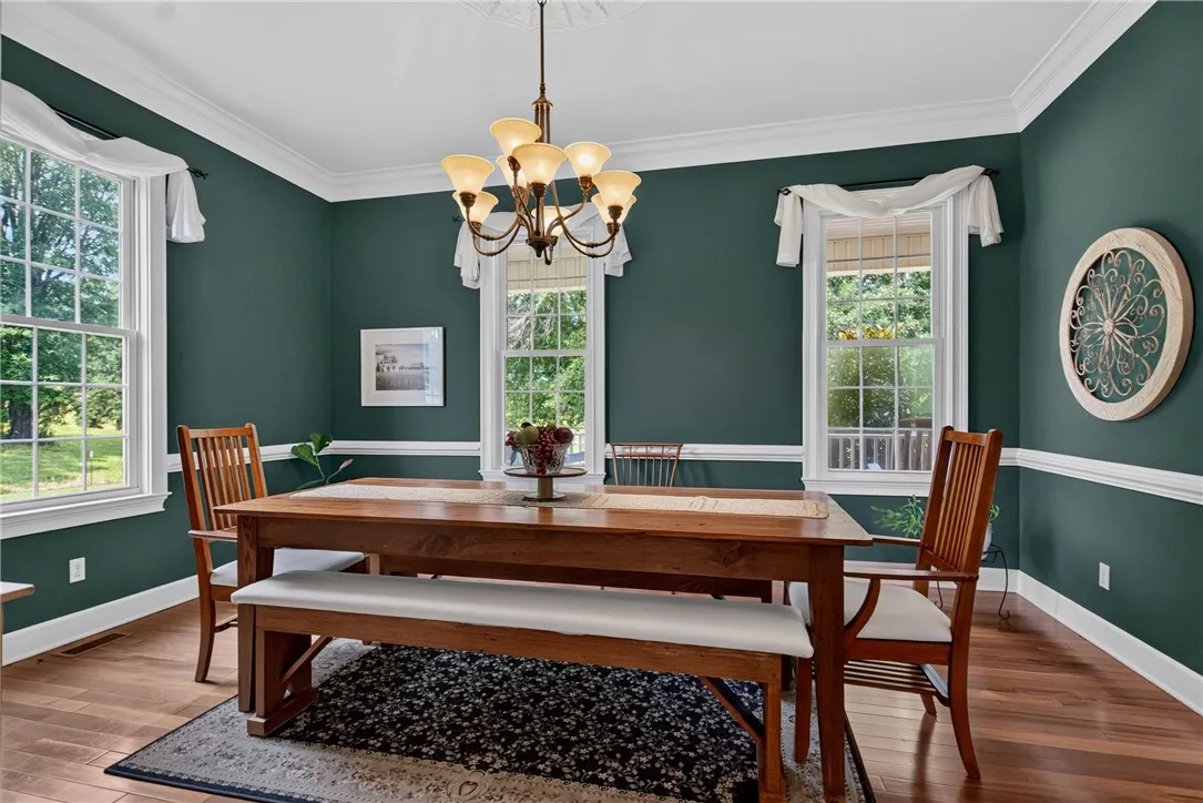 A well-lit dining area features lustrous hardwood flooring, elegant crown molding, and a charming chandelier.