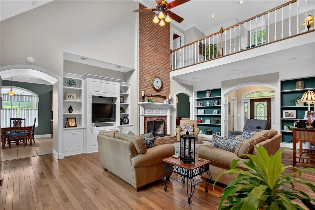 A spacious great room showcases soaring ceilings, a stately brick fireplace, and built-in shelving, with hardwood floors extending throughout.