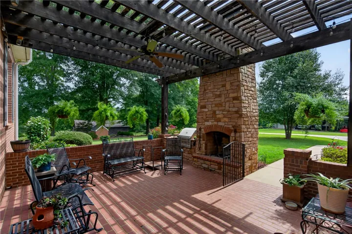 An inviting covered patio featuring a stone fireplace and brick flooring, ideal for outdoor gatherings.