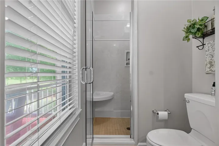 A window-lit lavatory features a walk-in shower with clear glass enclosure and corner sink.