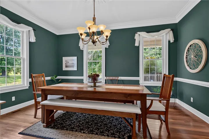 A well-lit dining area features lustrous hardwood flooring, elegant crown molding, and a charming chandelier.