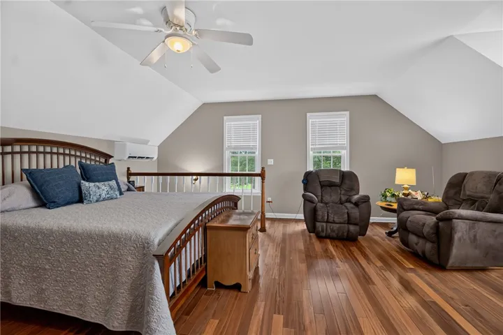 Hardwood floors and a vaulted ceiling elevate this primary bedroom's cozy aesthetic.