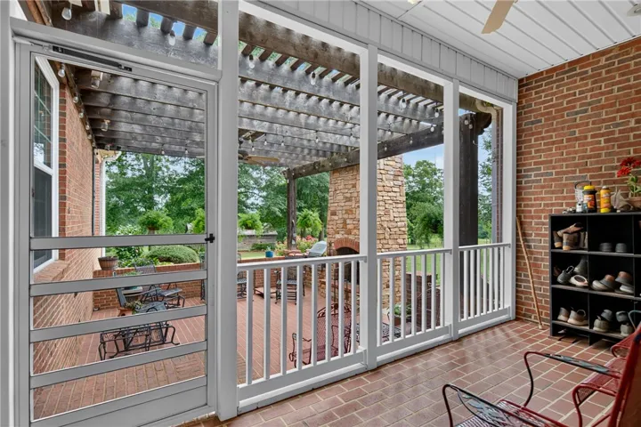 A spacious screened-in porch with brick flooring overlooks a stone patio and verdant backyard.