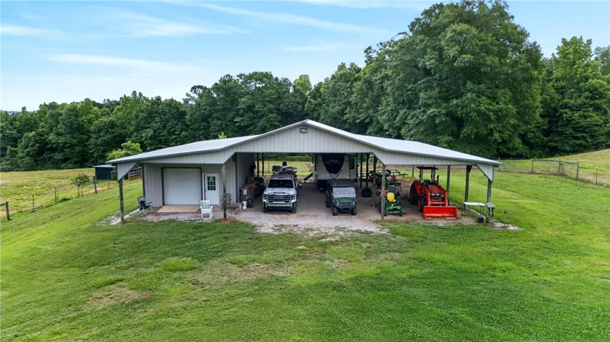 A spacious, open-sided barn with a metal roof offers ample covered parking and storage on a verdant, open lot.
